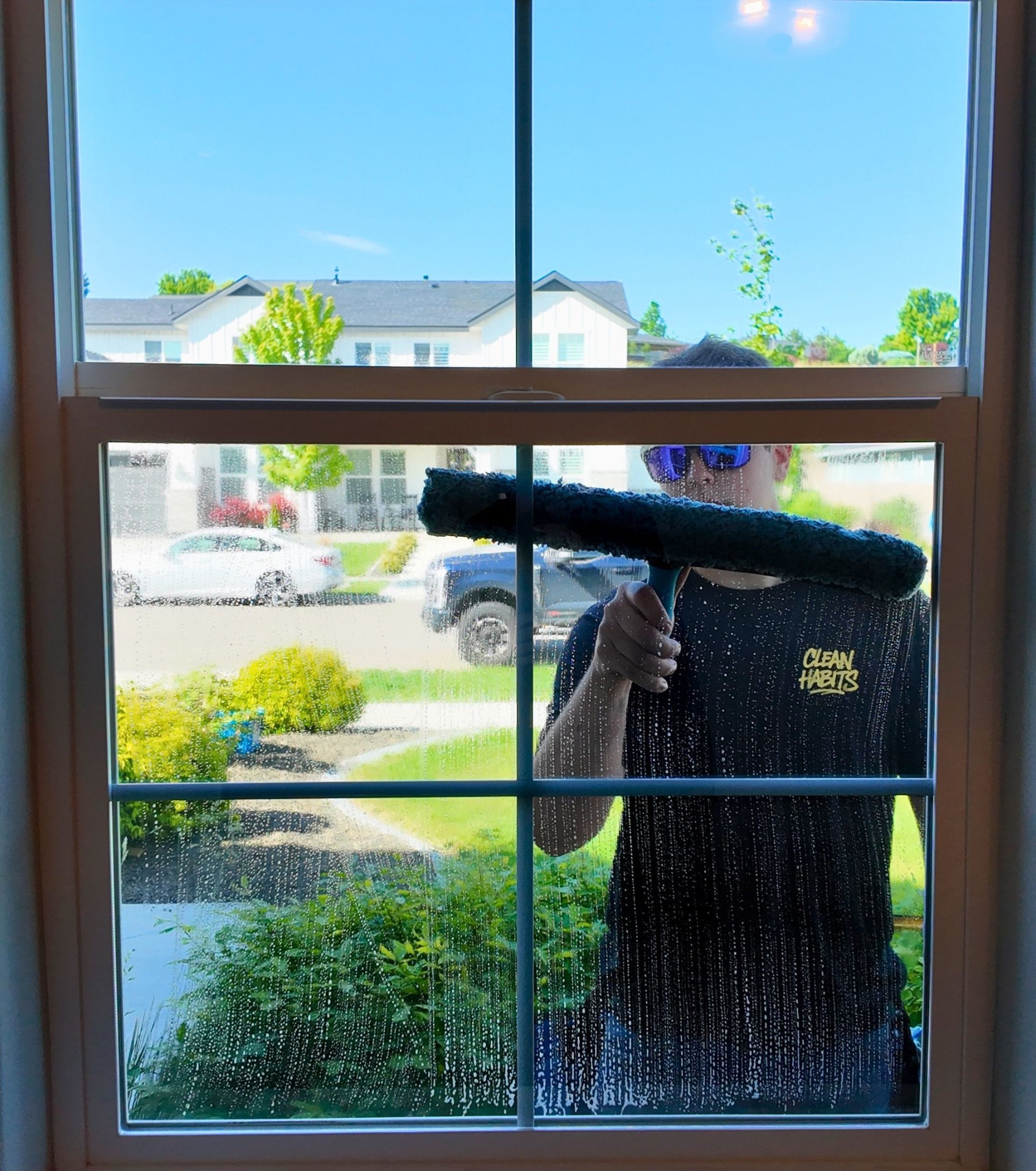 Sudz & Stripes technician squeegeeing the outside of a window, viewed from inside the home