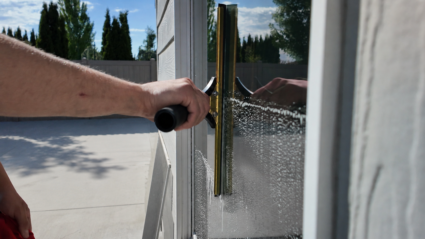 Close-up of a brass squeegee pulling a clean line down a soapy exterior window